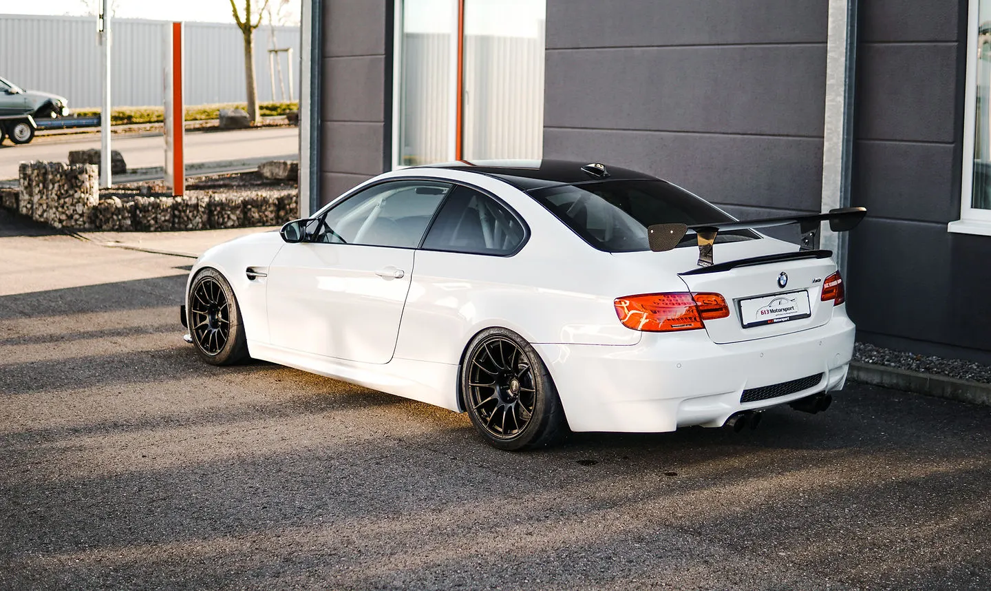 Weißer BMW M3 E92 mit Heckflügel und schwarzen Leichtmetallfelgen vor der Werkstatt von 613 Motorsport