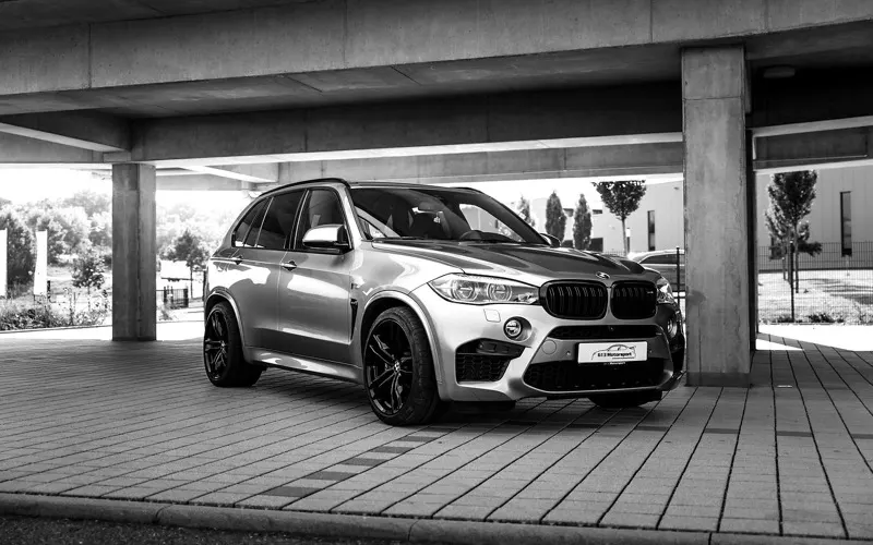 BMW X5 M mit schwarzen Felgen in Dreiviertelansicht unter einem Betonparkdeck