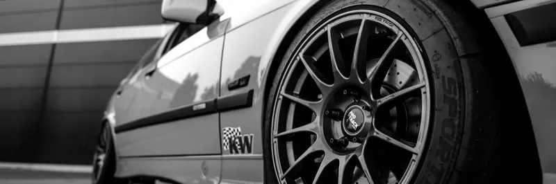 Nahaufnahme einer schwarzen Mehrspeichenfelge mit Semislick-Reifen an einem tiefergelegten BMW